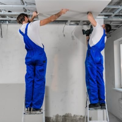 dwoch-pracownikow-wykonuje-sufit-z-plyt-gipsowo-kartonowych-uzywaja-wiertarki-i-drabin_225094-593